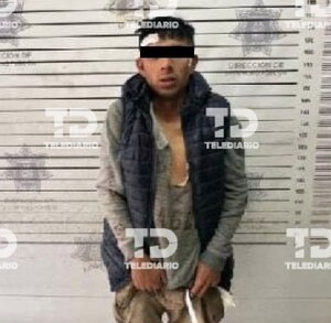 Un hombre con ojos tapados que usa una blusa gris y un chaleco negro.