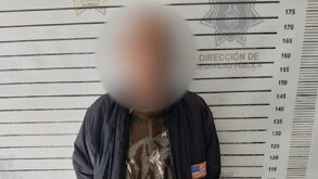 Hay un hombre con el rostro cubierto, que viste pantalón de mezcilla, zapatos café y chamarra azul.