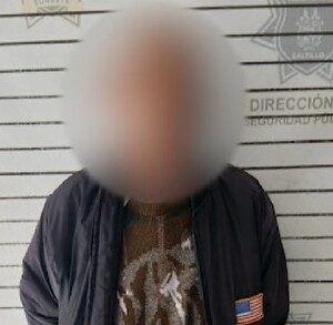 Hay un hombre con el rostro cubierto, que viste pantalón de mezcilla, zapatos café y chamarra azul.