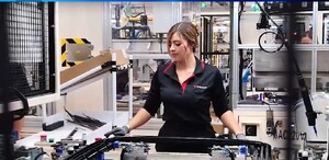 Se observa una mujer que está con unas máquinas, trae un pantalón y camisa negra.