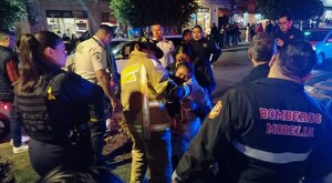 Bomberos y paramédicos de Morelia atendiendo a mujeres heridas con policías y personas alrededor en medio de la calle