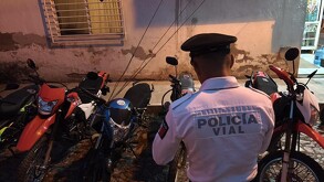 Un oficial de Policía Vial (uniforme blanco y gorra oscura) está de espaldas, de pie entre varias motocicletas de diferentes colores (rojo, blanco y azul)