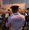 Un oficial de Policía Vial (uniforme blanco y gorra oscura) está de espaldas, de pie entre varias motocicletas de diferentes colores (rojo, blanco y azul)