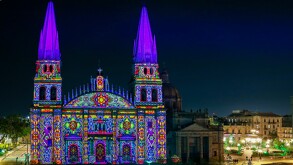 La Catedral de Guadalajara con sus torres gemelas está iluminada de noche con un patrón de luces de colores brillantes como magenta, verde, amarillo y azul.