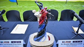 Una mesa con manteles negros y un trofeo central con figuras humanas de colores. Alrededor están los escudos de Chivas, Atlas, Rayados (Monterrey) y Leones Negr