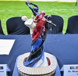 Una mesa con manteles negros y un trofeo central con figuras humanas de colores. Alrededor están los escudos de Chivas, Atlas, Rayados (Monterrey) y Leones Negr