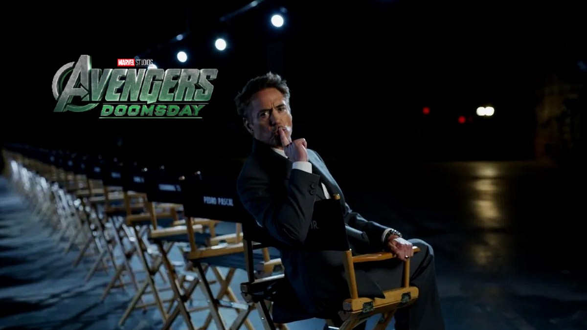 El actor Robert Downey Jr. (traje oscuro, mano en la barbilla) está sentado en una silla de director en un estudio oscuro. En la esquina superior izquierda se l