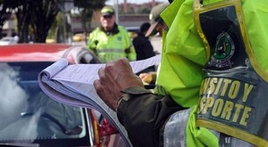 Oficiales de tránsito en Michoacán sosteniendo documentos de infracción al lado de un automóvil rojo con otro oficial y personas detrás