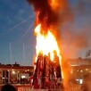 A la izquierda: árbol de Navidad ardiendo en llamas en plaza pública. A la derecha: vista desde otro punto del incendio del árbol de Navidad con gente alrededor