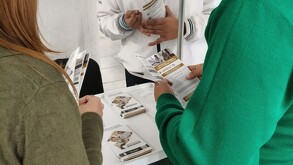 Tres personas, vestidas de manera informal, están de pie alrededor de una mesa examinando folletos informativos sobre el 