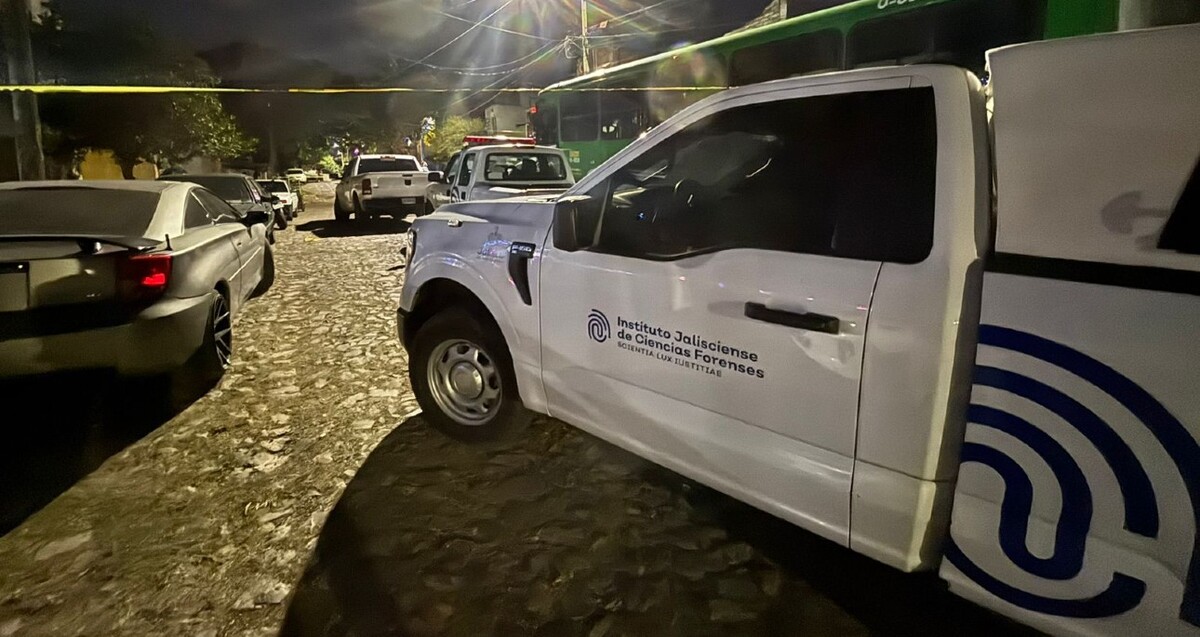 Camioneta del Instituto Jalisciense de Ciencias Forenses estacionada detrás de diversos automóviles y al lado de un camión verde durante la noche