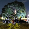 Vecinos reunidos con policías a las afueras de una casa con autos estacionados alrededor de un árbol de gran tamaño durante la noche