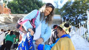 una mujer le entrega una mochila a un niño frente a una escuela