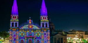 La Catedral de Guadalajara con sus torres gemelas está iluminada de noche con un patrón de luces de colores brillantes como magenta, verde, amarillo y azul.
