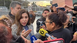 Se observa a una mujer vestida con saco blanco con negro y algunas personas con micrófonos.