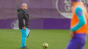 El político Enrique Alfaro (con chamarra deportiva negra y pantalón azul claro) observa un entrenamiento de fútbol en una cancha de césped.
