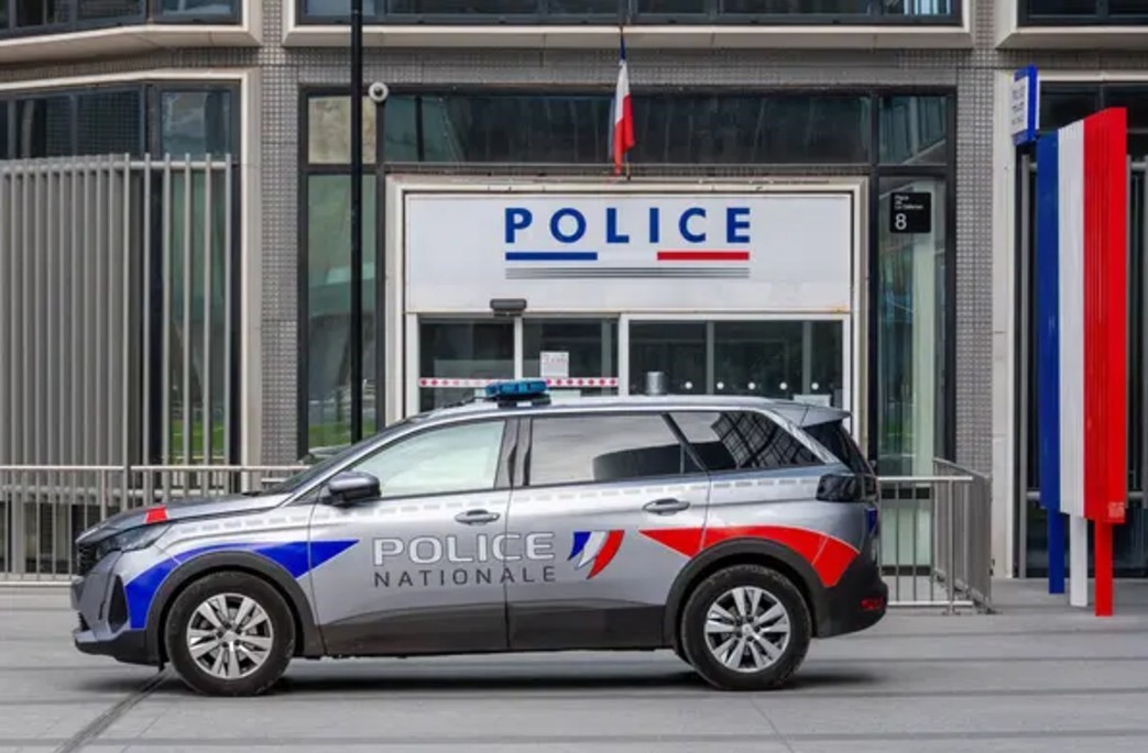 Patrulla de la Policía Nacional de Francia estacionada frente a una estación policial con banderas del país colocadas en diversos puntos