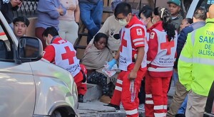 Paramédicos de la Cruz Roja y SAMU Jalisco atendiendo a heridos con vecinos alrededor abrazando a una señora al exterior de una casa