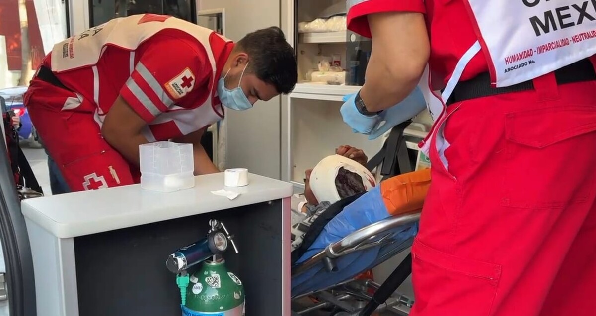 Paramédicos de la Cruz Roja con cubrebocas y guantes atendiendo a un hombre herido de la cabeza dentro de una ambulancia