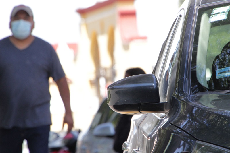 Un hombre usando cubrebocas y gorra mira fijamente un vehículo, con la intención de robarlo.