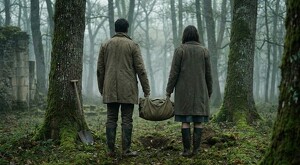 Pareja de hombre y mujer vistos de espaldas sosteniendo un bulto y a punto de enterrarlo en medio de un bosque