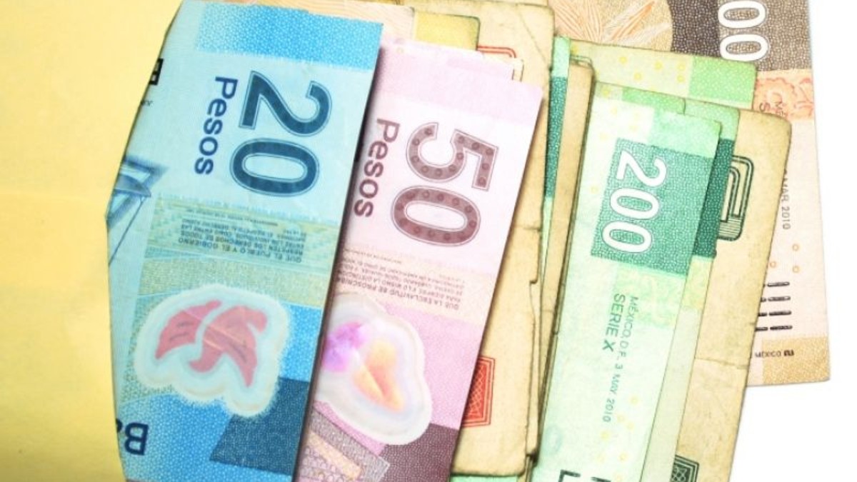 Un fajo de billetes de pesos mexicanos de diversas denominaciones sobresale de un sobre amarillo. Se ven claramente uno azul de $20$, uno rosa de $50$