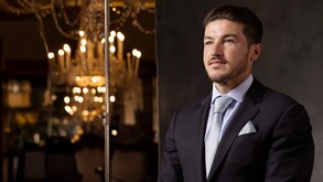 Samuel García en primer plano retratado de traje con un fondo lámparas