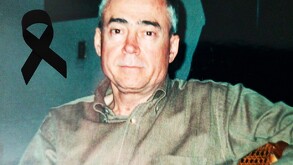 Se observa a un hombre con canas que viste una camisa color verde y hay un moño negro.