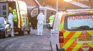 Vista trasera de un vehículo forense de Inglaterra con médicos y policías detrás junto a una patrulla de policía y casas alrededor