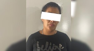 Mujer viendo de frente con los ojos censurados por un cuadro blanco, vistiendo una playera negra frente a una pared café