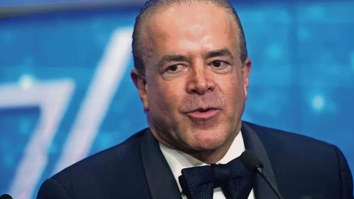 Fotografía de Raúl Rocha con un fondo azul y usando un traje negro.