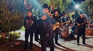 Julión Álvarez con músicos detrás, viendo de frente y apuntando a la cámara mientras canta en la posada de la Secretaría de Seguridad de Jalisco