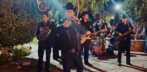 Julión Álvarez con músicos detrás, viendo de frente y apuntando a la cámara mientras canta en la posada de la Secretaría de Seguridad de Jalisco