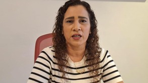 Mujer vestida con una playera blanca con rayas, hablando frente a la cámara.