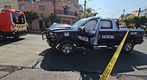 Patrulla de la Secretaría de Seguridad de Jalisco con múltiples abolladuras y una puerta abierta estacionada detrás de una ambulancia de la Cruz Roja