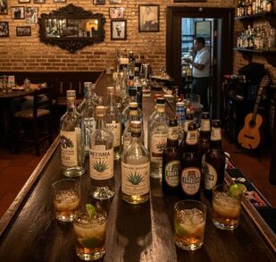 En la imagen se observan bebidas embriagantes en una barra, y al fondo un hombre.