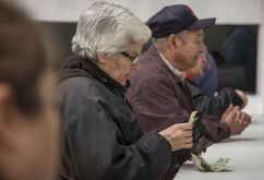 Se observa a unos adultos mayores con dinero enfrente de unas ventanillas.