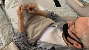 Se observa a un hombre canoso con un cubrebocas negro, firmando unos papeles.