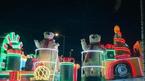 Carro alegórico de la caravana navideña con dos osos polares gigantes con bufandas rojas, luces de neón verdes y rojas, y adornos de regalos.