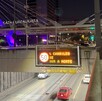 Letrero electrónico nocturno sobre un túnel indica '5 CARRILES DE SUR A NORTE'. De fondo destaca el puente Matute Remus con luces púrpuras.