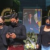 Personas de negro y con cubrebocas caminan frente a un retrato de Aristóteles Sandoval rodeado de coronas florales en lo que parece un memorial.