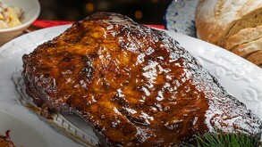 Se observa un corte de carne servido en un plato blanco, con pan a lado y unas hierbas verdes.