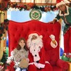 Santa Claus sentado en un gran trono rojo con una niña y un duende en un set navideño decorado con guirnaldas del Zoológico Guadalajara.
