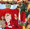 Santa Claus sentado en un gran trono rojo con una niña y un duende en un set navideño decorado con guirnaldas del Zoológico Guadalajara.