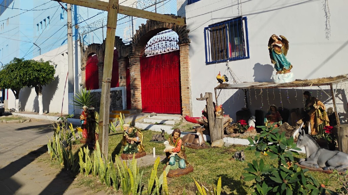 Fachada de un edificio de dos niveles pintado en colores naranja y amarillo vibrantes, con grandes ventanales y un portón metálico con símbolos.