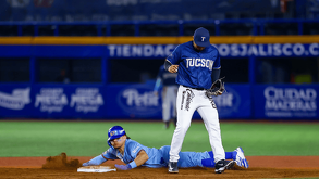 Jugador de béisbol de los Charros de Jalisco se desliza en una base mientras el oponente espera la bola durante un juego nocturno en el estadio.