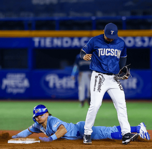 Jugador de béisbol de los Charros de Jalisco se desliza en una base mientras el oponente espera la bola durante un juego nocturno en el estadio.