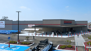 Fachada exterior de una sucursal de Costco Wholesale con un amplio estacionamiento, señalización azul para personas con discapacidad y un cielo despejado.