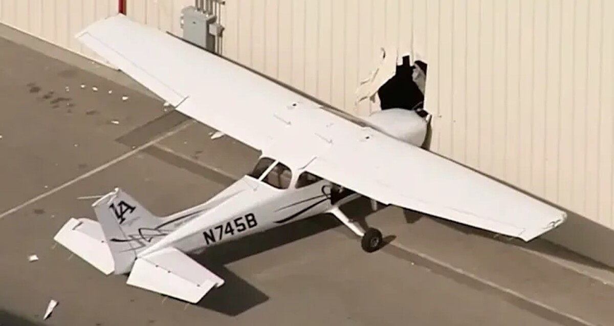 Vista cenital de una aeronave blanca tipo Cessna C172 estrellada de la parte delantera contra un muro en un aeropuerto de EU