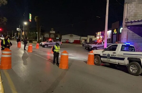 Se observa a unos policías de tránsito en la vialidad y a unos carros en tránsito.